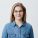 Horizontal portrait of smiling happy young pleasant looking female wears denim shirt and stylish glasses, with straight blonde hair, expresses positiveness, poses against gray background with copy space for promotional text